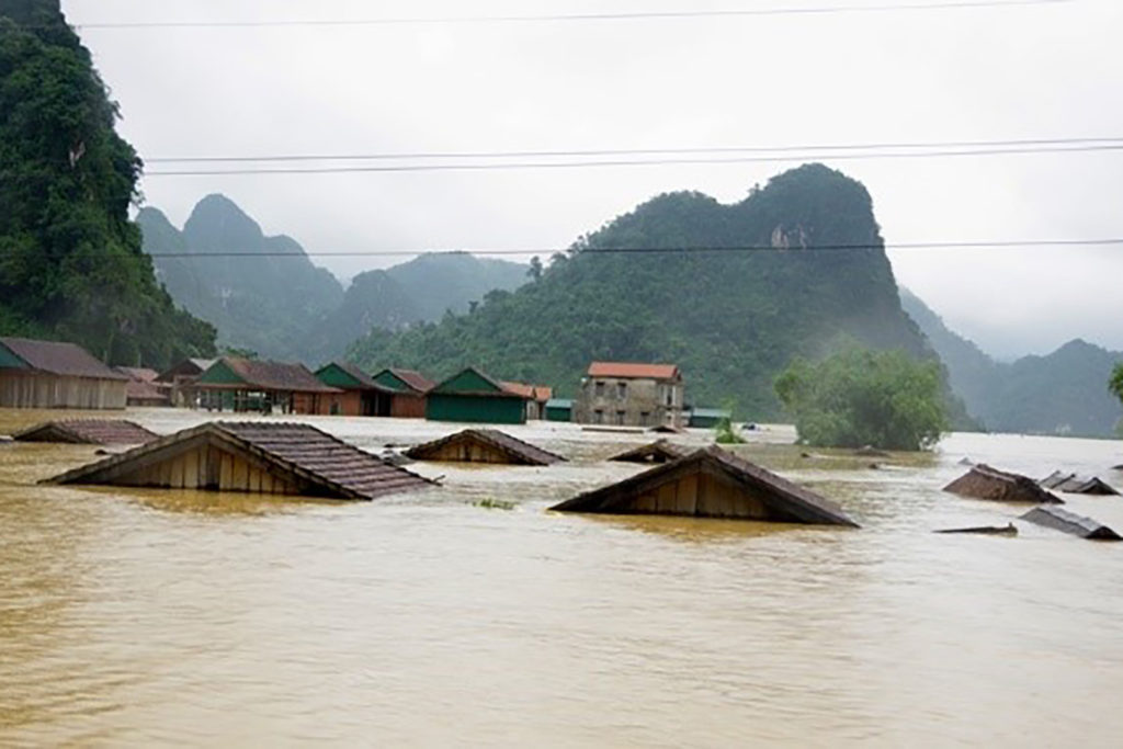 Water from a flood with the roofs of houses showing. Houses on higher land and tree covered hills in the background