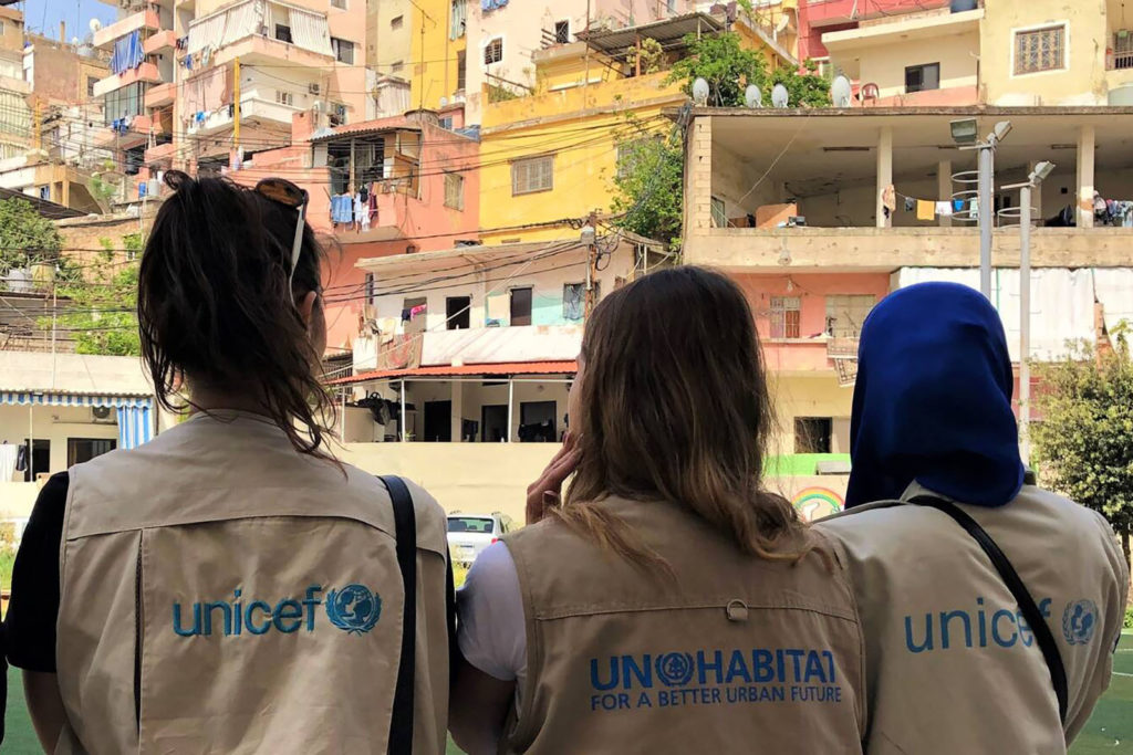 Three people wearing UNICEF vests looking at apartment dwellings