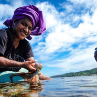 Two women with brightly coloured fabric on their heads are fishing using their hands