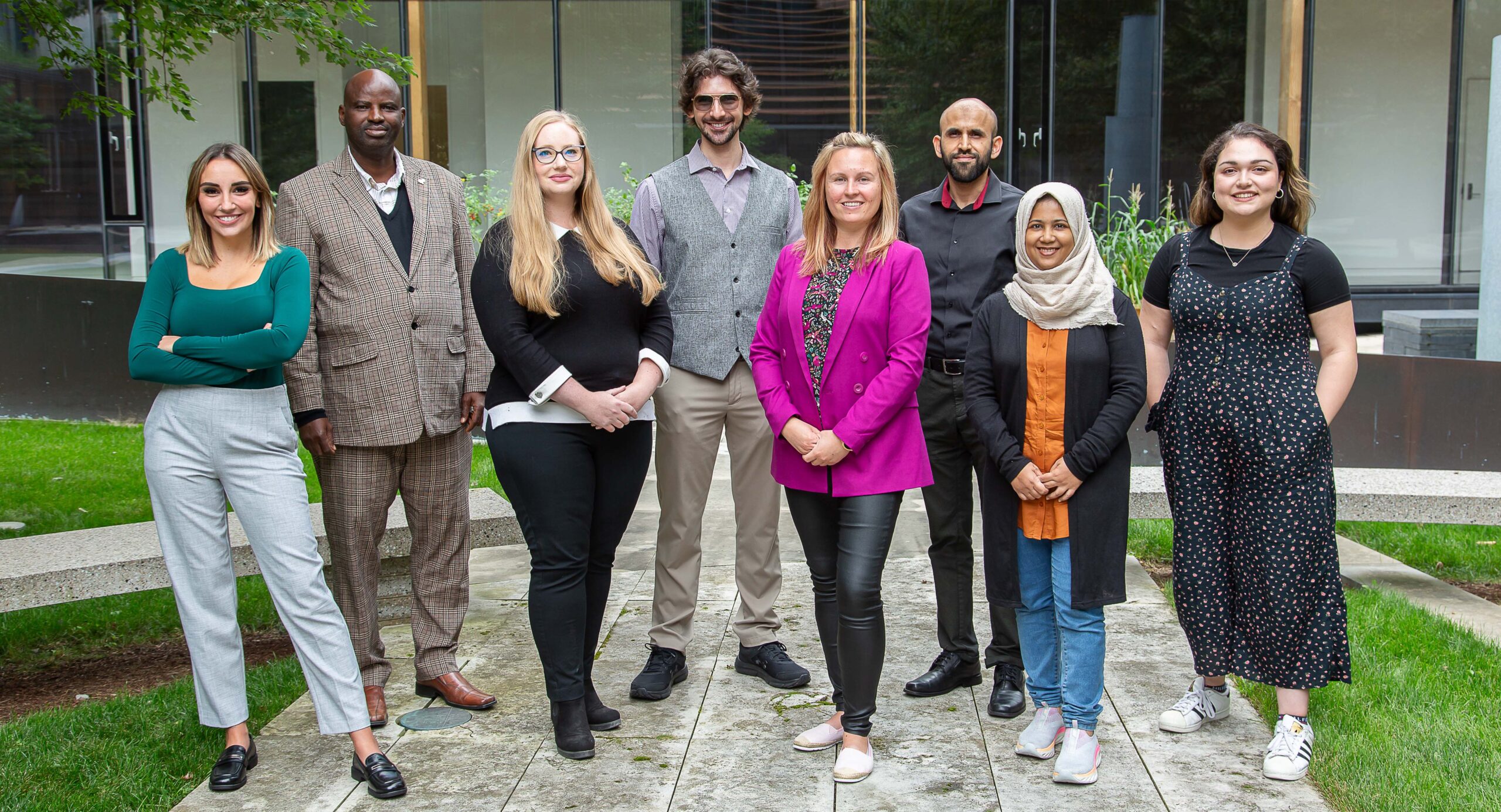Eight PhD students standing together with a building windows behind them.