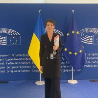 Halyna Padalko standing in front of a EU parliament banner with the Ukraine and EU flag behind her.